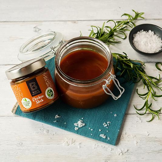 An open kilner jar of Bay's Kitchen Chicken stock on a mat with salt and rosemary